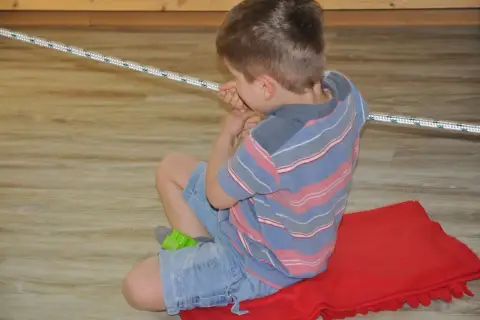 Chłopiec ćwiczy obniżone napięcie mięśniowe w jamie ustnej, bawiąc się sznurkiem.